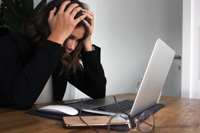 A person looking frustrated at a calculator and a stack of bills, with a simple, bare-bones grocery bag in the background.